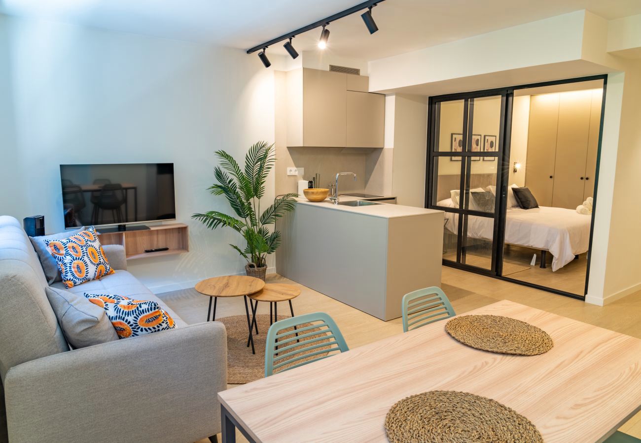 Salón con sofá y cojines de color, mesa de comedor y cocina en isla al fondo