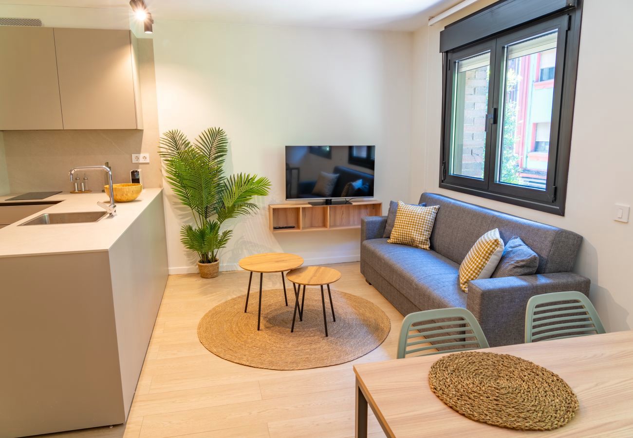 Salón luminoso con sofá y mesas nido junto a la cocina abierta