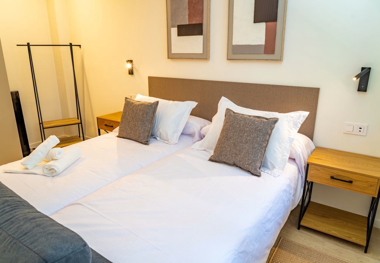 Rincón de descanso con silla de mimbre y sofá cama junto a la ventana, Urban Estudio