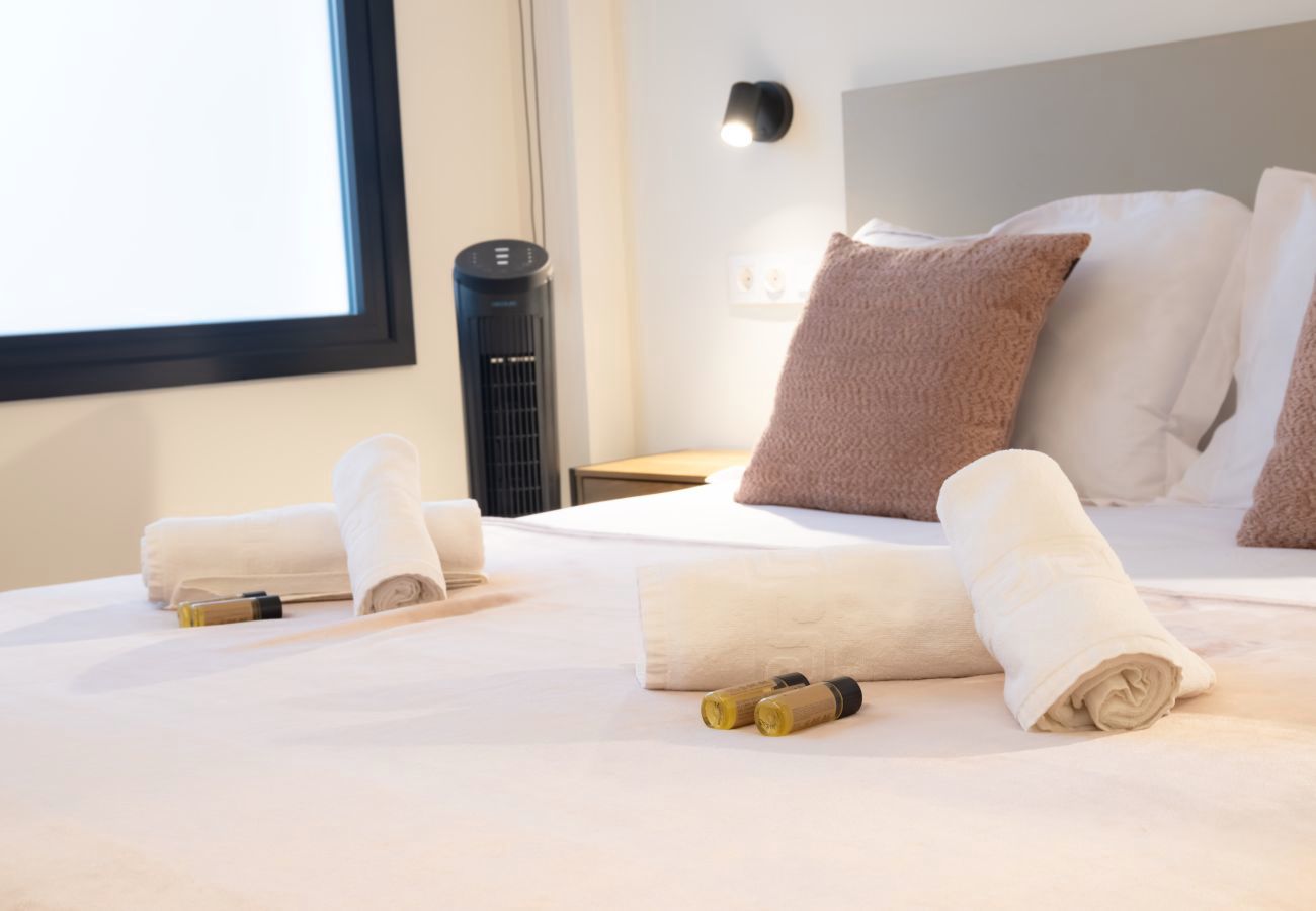 Detalle de toallas enrolladas y amenities sobre la cama, apartamento Urban Plus