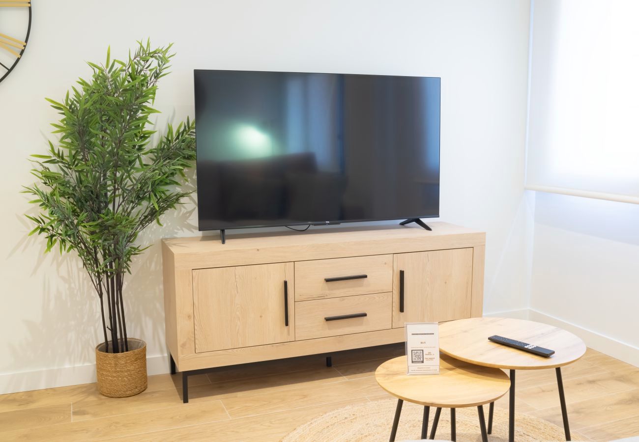 Salón con televisor sobre mueble de madera y mesas nido, apartamento Urban Plus