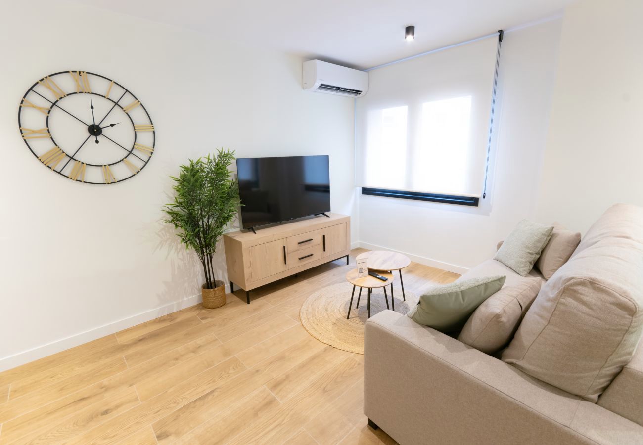 Salón con reloj de pared grande y televisor, apartamento Urban Plus