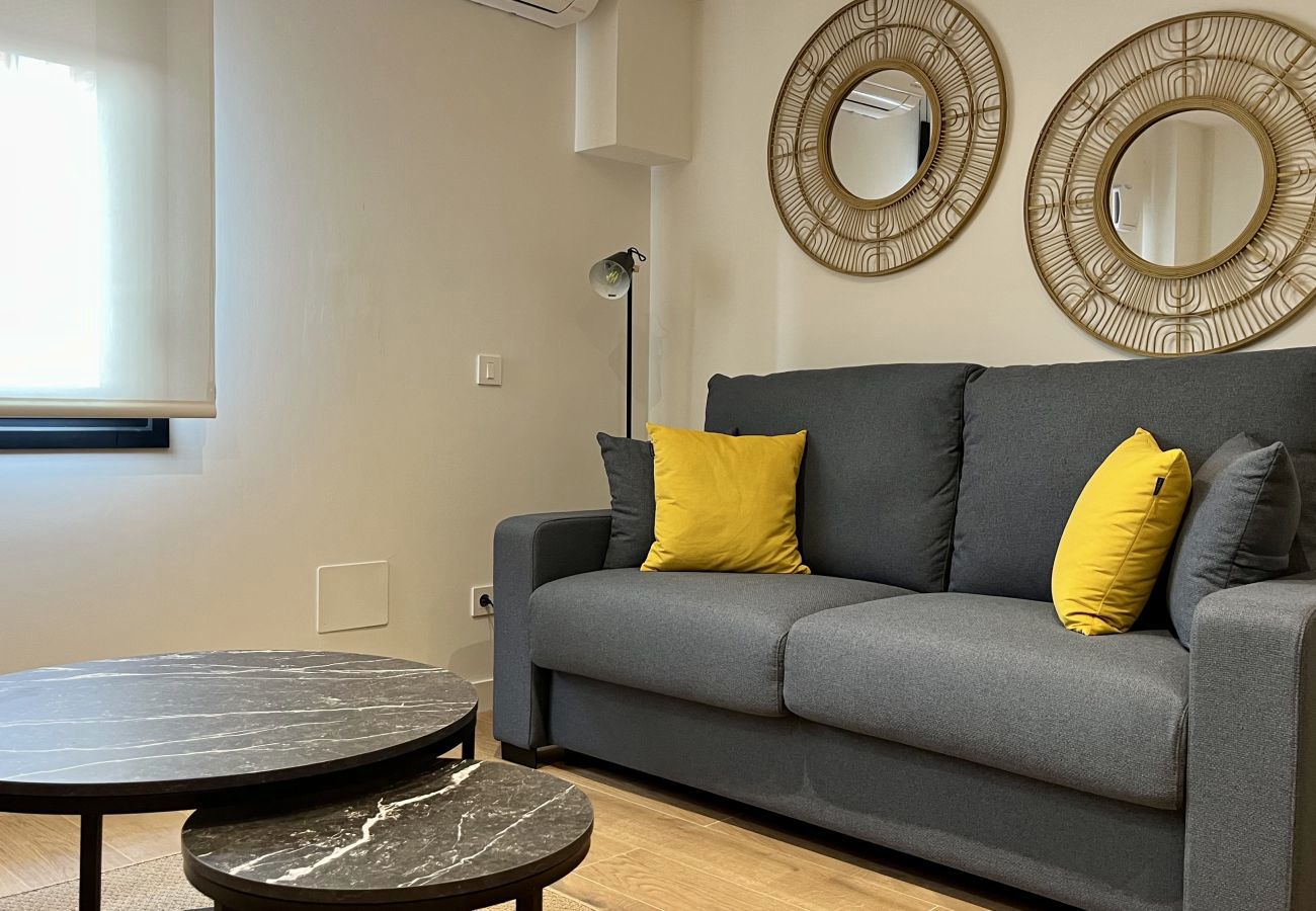Salón con sofá gris, cojines mostaza y mesas de centro negras, Urban Premium