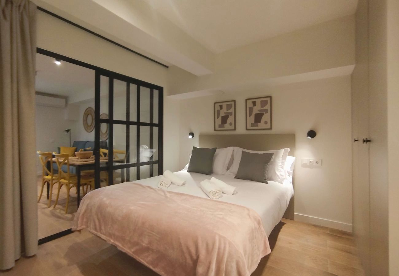 Dormitorio con manta rosa palo y vista al comedor tras la puerta de cristal, Urban Premium