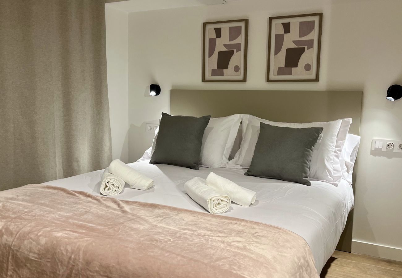 Dormitorio con cabecero verde oliva y cojines grises, apartamento Urban Premium