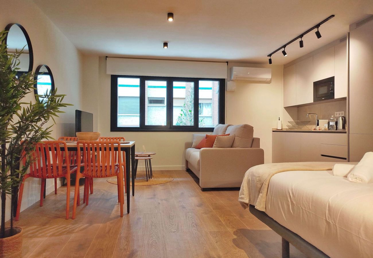 Estudio con sillas terracota, sofá y cama al fondo, apartamento Urban Suite