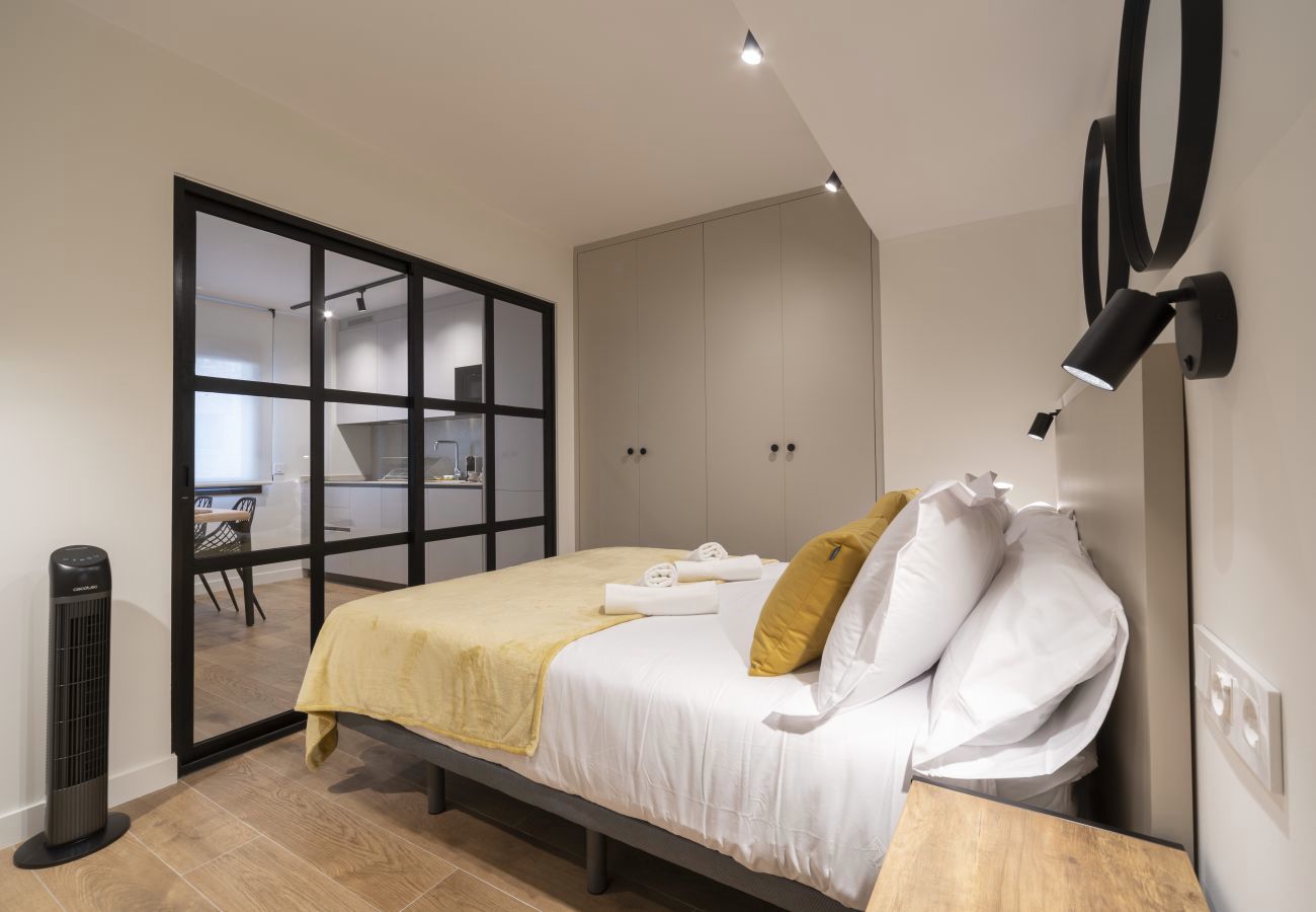 Dormitorio con manta mostaza y puerta corredera de cristal a la cocina, Urban Suite
