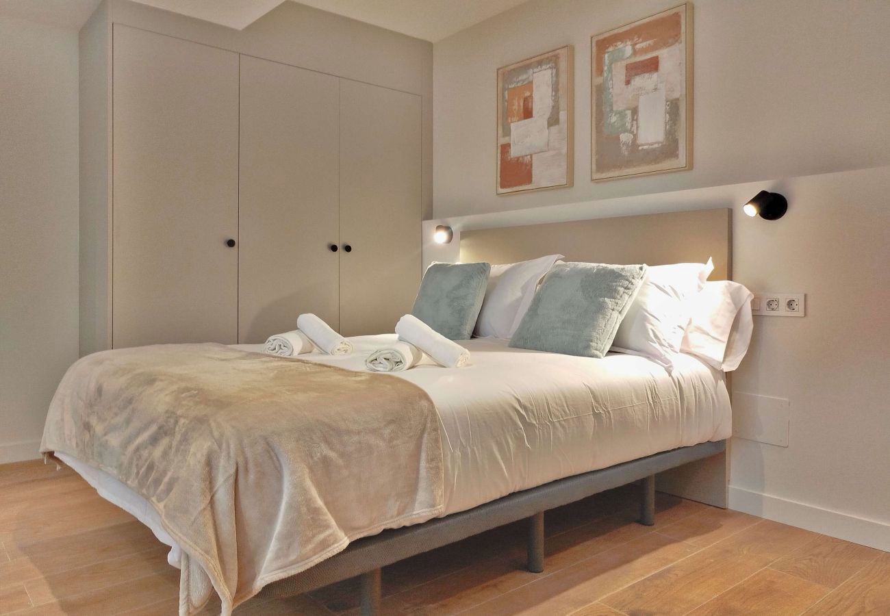 Dormitorio con cojines verde salvia y manta beige, apartamento Urban Suite