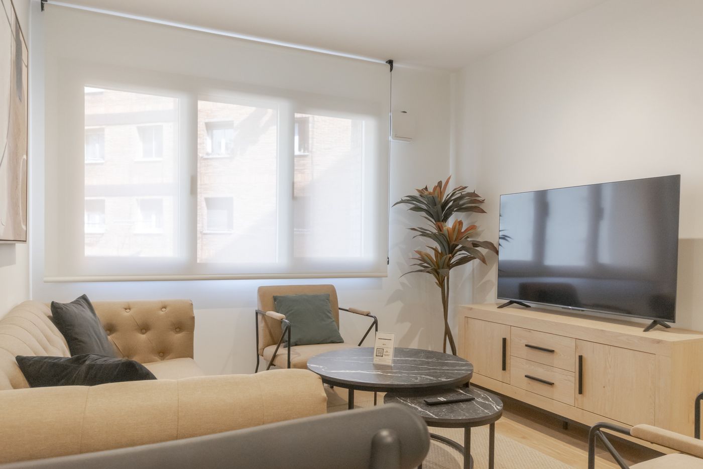 Salón con sofá beige, sillón y televisor sobre mueble de madera, apartamento Urban Superior