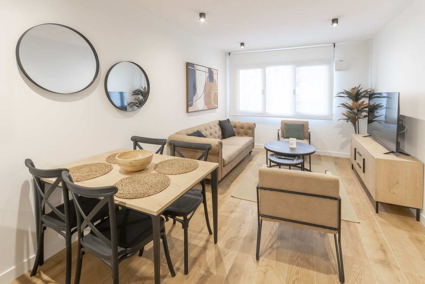Mesa de comedor de madera con espejos redondos y sofá al fondo, apartamento Urban Superior