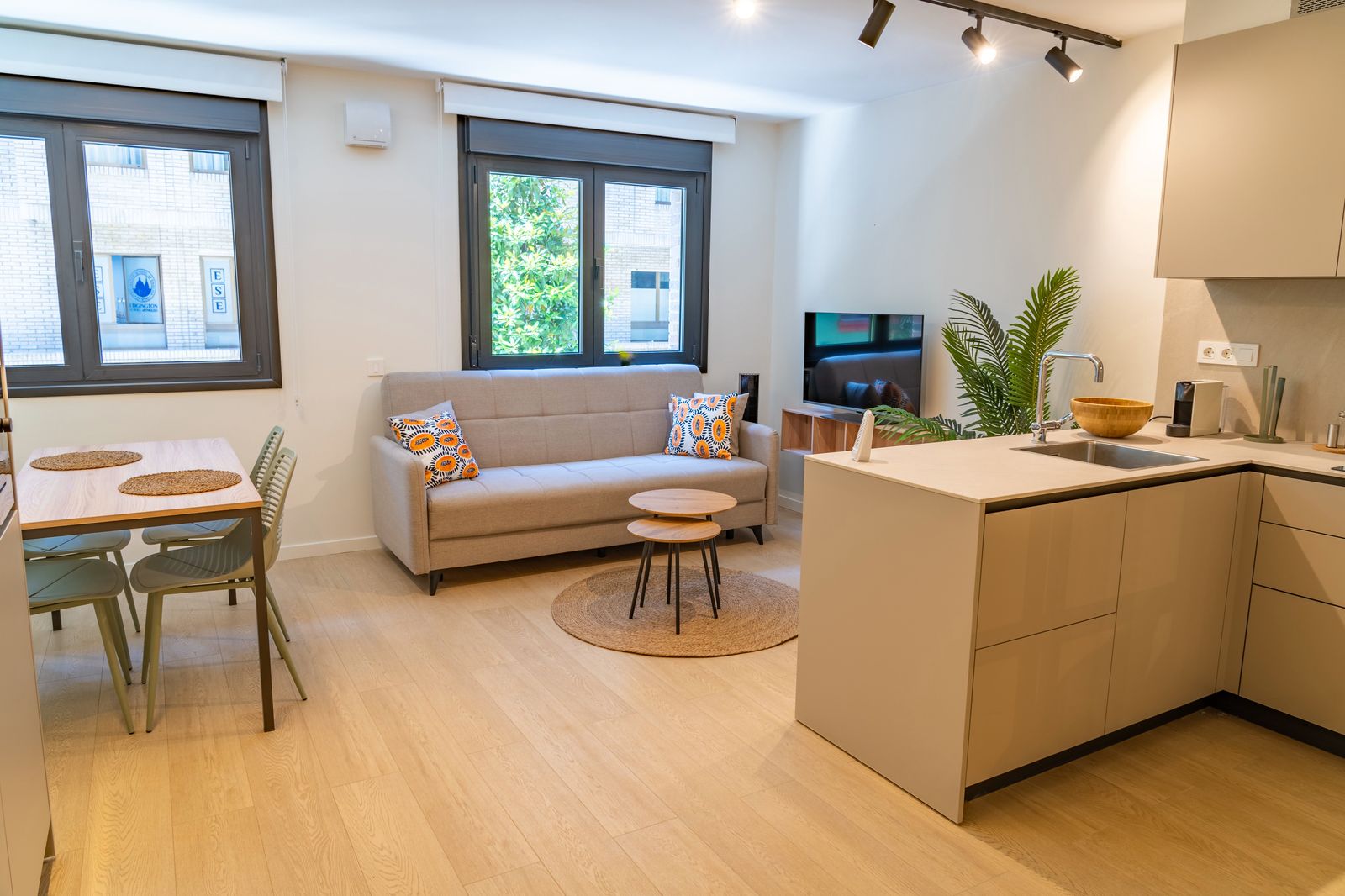Salón con sofá gris, cojines de color y cocina abierta luminosa